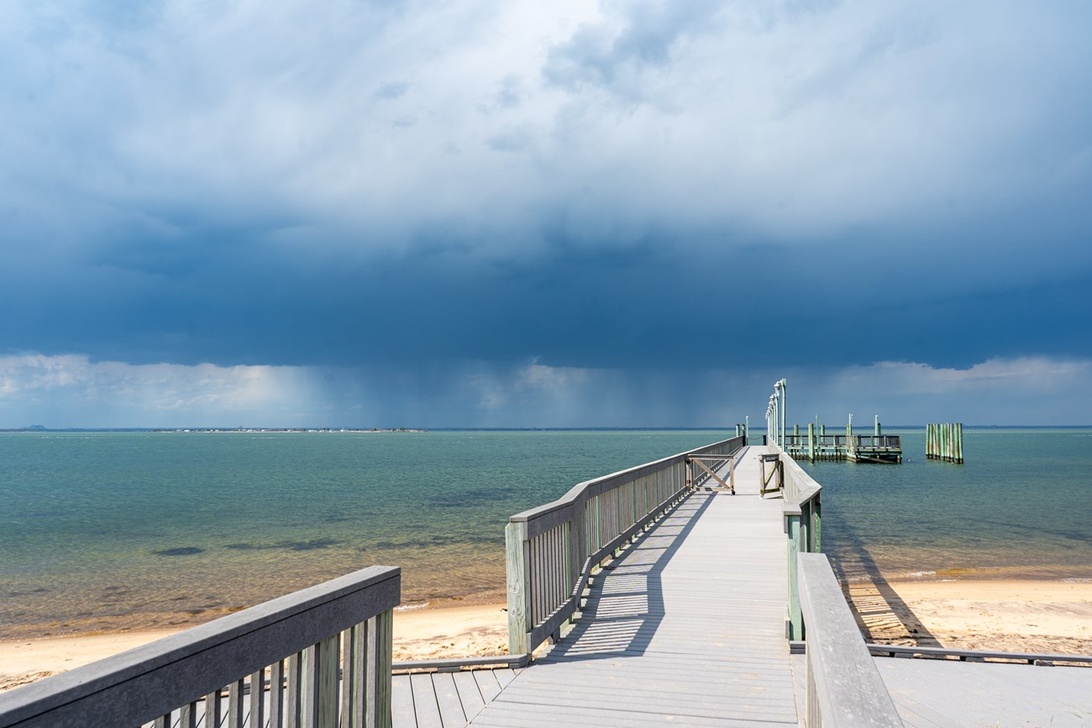 En trebrygge strekker seg ut i rolige bukt under en stormfull himmel, et ideelt klekkeområde for saltvannsmygg.