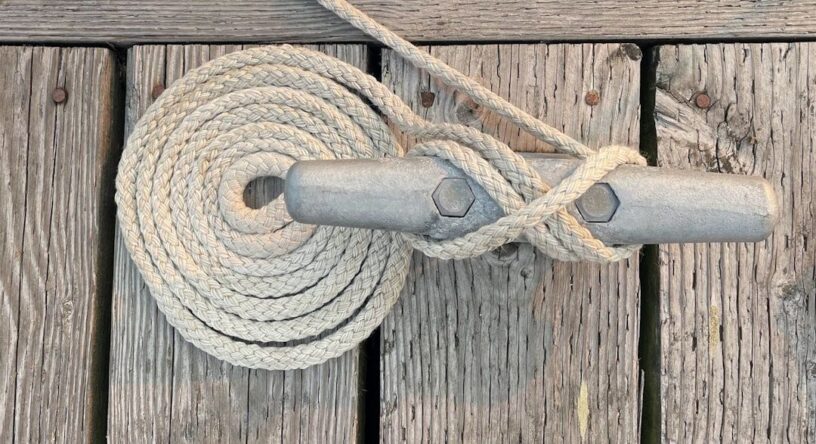 Tykt fortøyningstau surret rundt en metallpullert på trebrygge