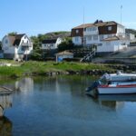 Båter ligger fortøyd i en rolig vik foran hus på svaberg