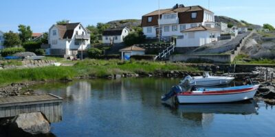 Båter ligger fortøyd i en rolig vik foran hus på svaberg