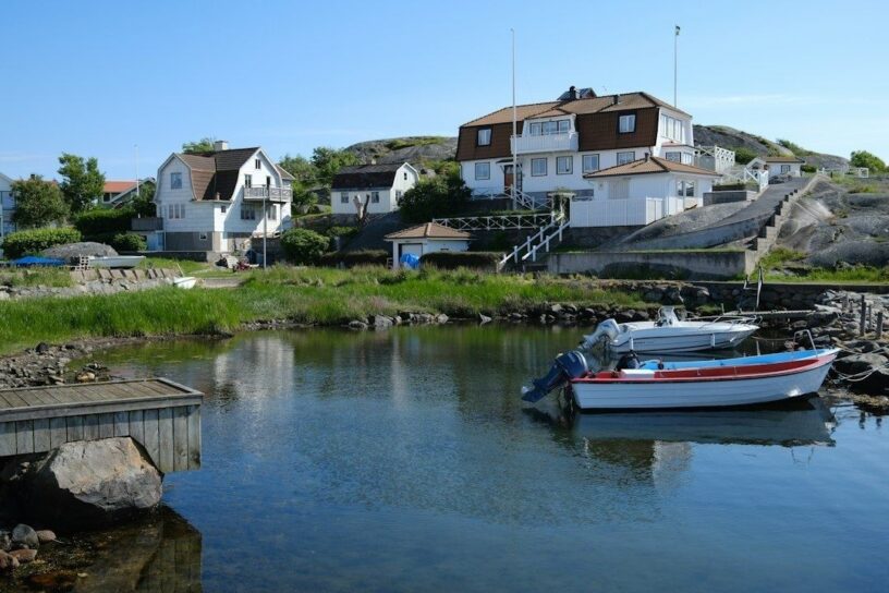 Båter ligger fortøyd i en rolig vik foran hus på svaberg